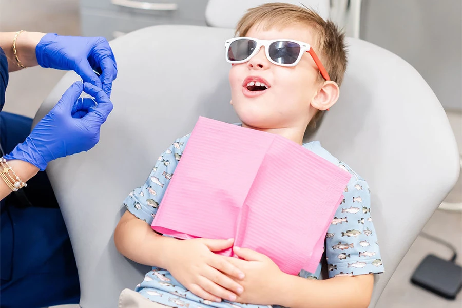 Young boy wearing sunglasses smiling in dental chair at Malbis Parkway Pediatric Dentistry