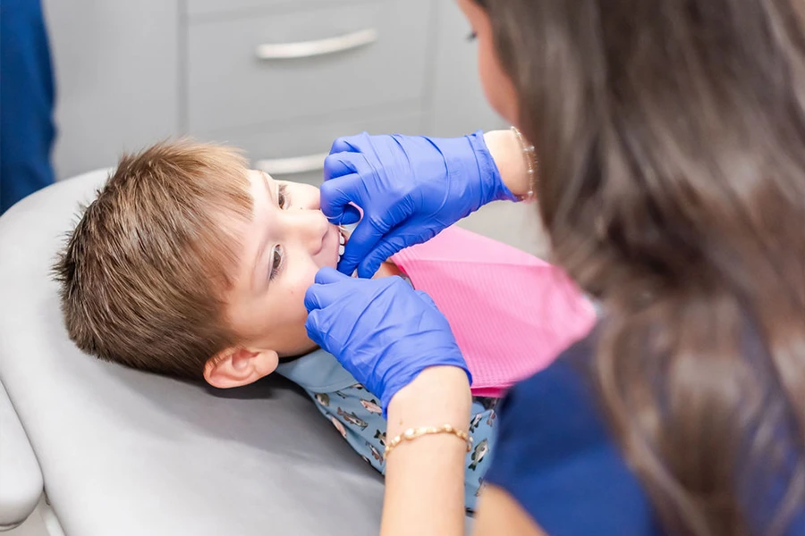 Gloved dental team member examining smiling young boy's teeth