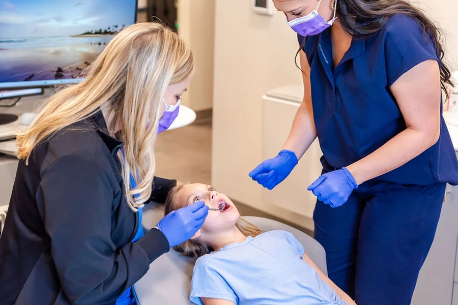 Two dental team members performing exam on young girl patient together