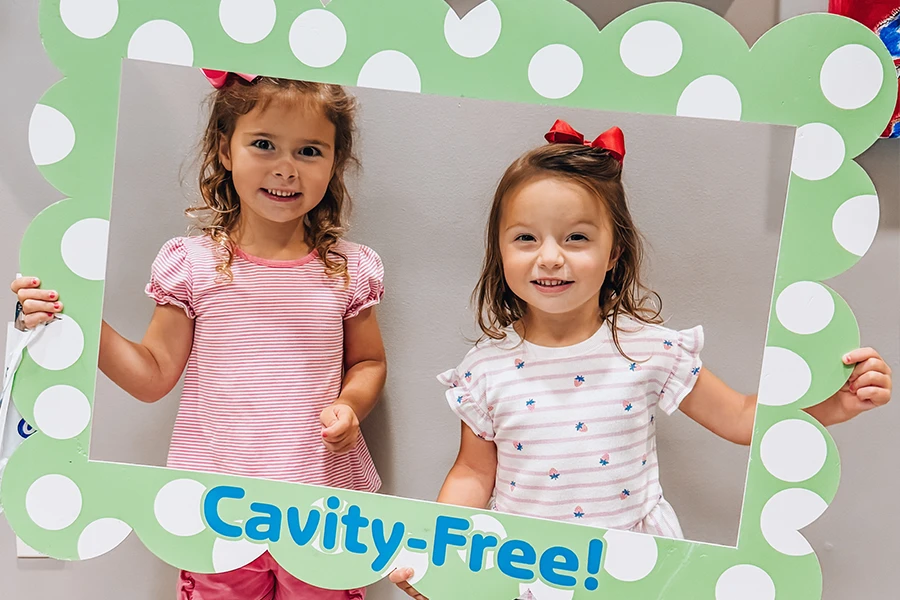 Two young girls holding Cavity-Free photo frame at pediatric dentist