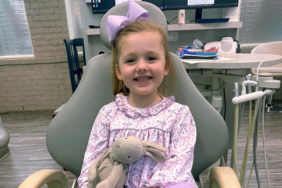 Smiling young girl holding stuffed bunny in pediatric dental chair
